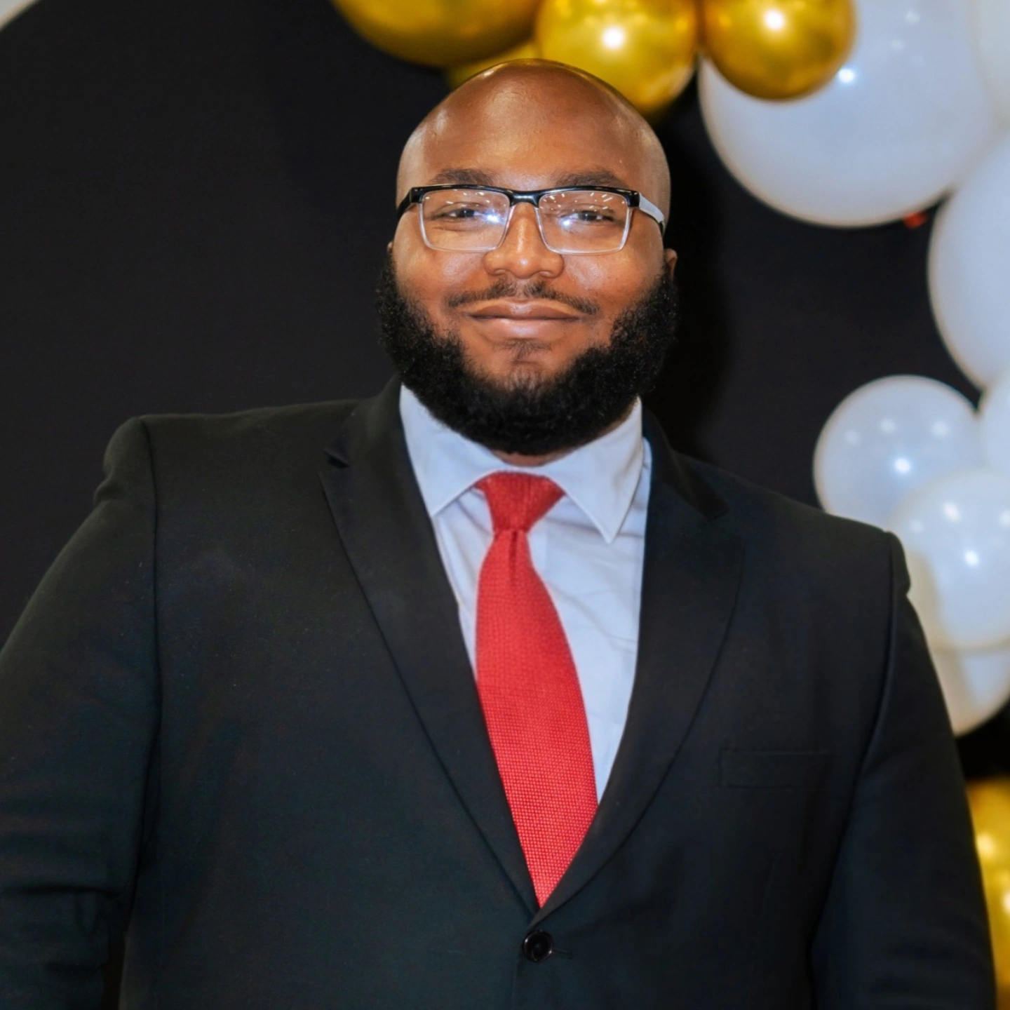 Prince Flye, founder of F.A.T.E., smiling in a dark suit and red tie